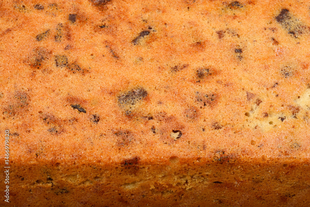 The textured surface of a freshly baked loaf cake with walnuts, raisins, chocolate pieces, and orange zest
