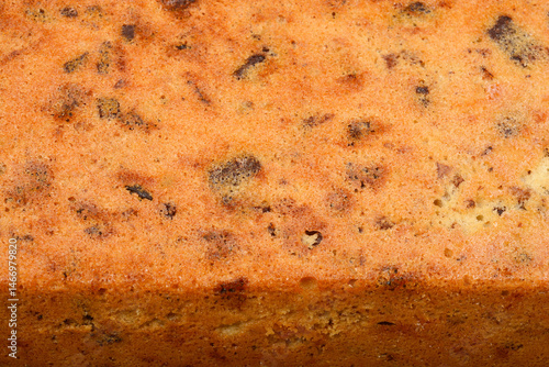 The textured surface of a freshly baked loaf cake with walnuts, raisins, chocolate pieces, and orange zest