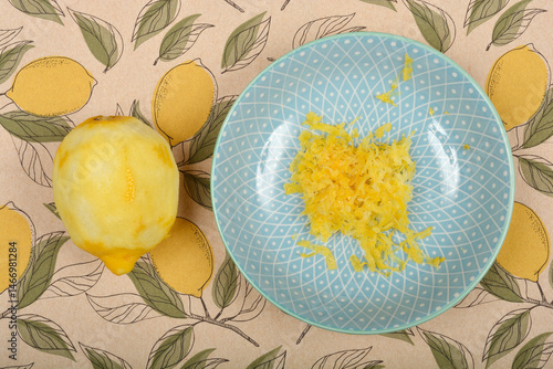 Obraz na płótnie A whole peeled lemon lies next to a light blue patterned plate containing lemon zest, on a lemon-themed tablecloth w salonie