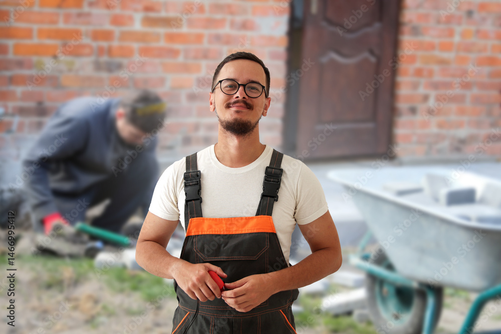 Smiling construction worker in overalls with a tape measure, building a patio outside. Landscape designer at work. Landscape design project