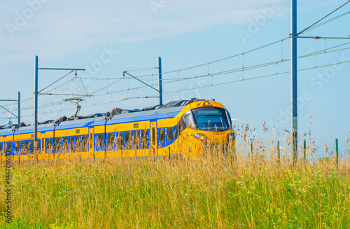 Electric train riding on a railroad track in nature in sunlight in springtime, Oostvaardersplassen, Almere, Flevoland, The Netherlands, May 8, 2025