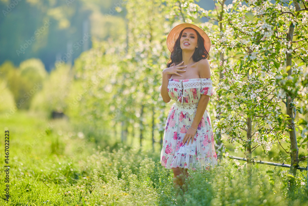 Full body portrait of a beautiful woman in a dress in a blooming apple orchard on a sunny spring day