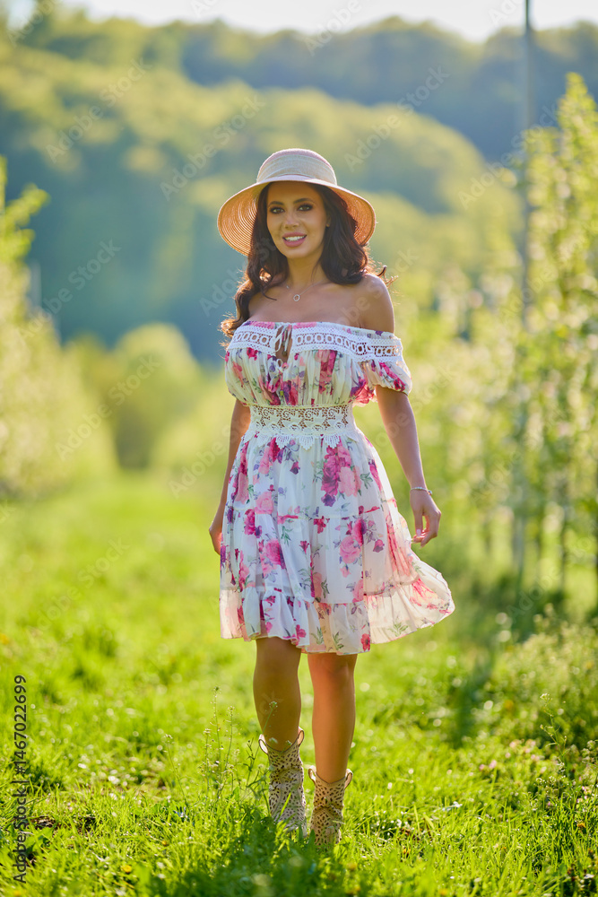 Full body portrait of a beautiful woman in a dress in a blooming apple orchard on a sunny spring day