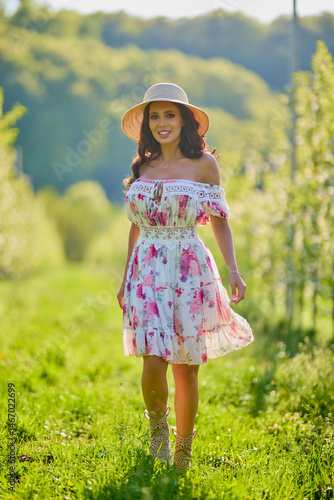 Obraz na płótnie Full body portrait of a beautiful woman in a dress in a blooming apple orchard on a sunny spring day w salonie