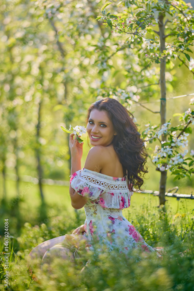 portrait of a beautiful woman in a dress in a blooming apple orchard enjoying a sunny spring day