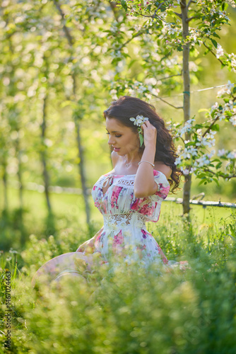 portrait of a beautiful woman in a dress in a blooming apple orchard enjoying a sunny spring day