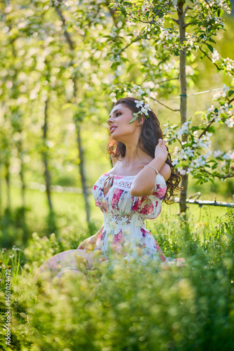 portrait of a beautiful woman in a dress in a blooming apple orchard enjoying a sunny spring day