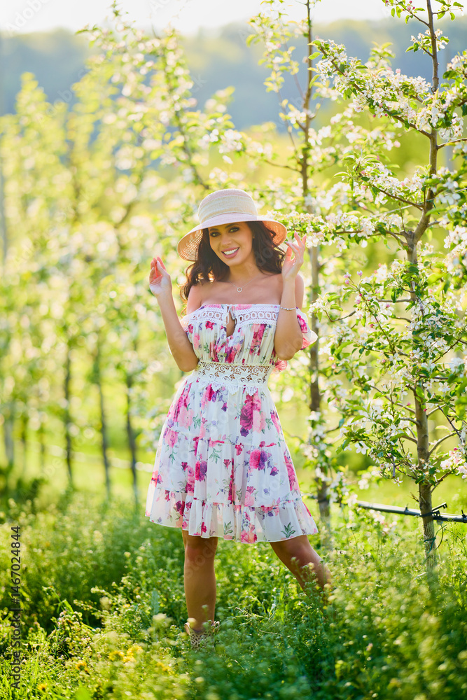 Full body portrait of a beautiful woman in a dress in a blooming apple orchard on a sunny spring day