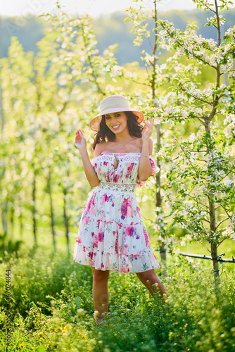 Full body portrait of a beautiful woman in a dress in a blooming apple orchard on a sunny spring day