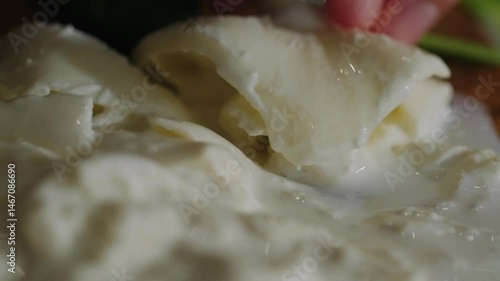 Cutting burrata close-up. The knife slowly makes a cut in the freshest burrata and the delicate cream begins to flow out onto the wooden board. Young craft cheese, еnjoyment from food.