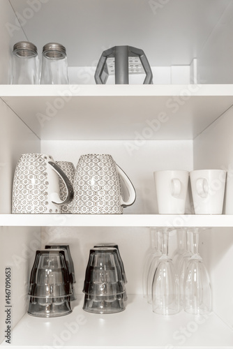 Kitchen cupboard with different clean dinnerware. Shelving with dishes, glasses and cups.