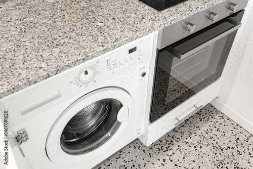 Принти на полотні Close-up view of a modern kitchen interior featuring a built-in washing machine and an electric oven under a granite countertop
