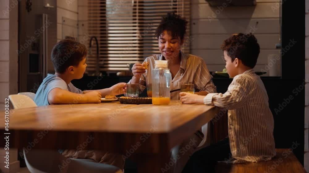 The son sits at the table and gives a piece of pie to his mother who bites it, next to them sits his brother who drinks from a glass The son sits at the table and gives a piece of pie to his mother who bites it, next to them sits his brother who drinks from a glass