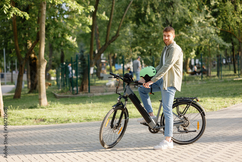 Man enjoys biking in a park on a sunny day while wearing a helmet and smiling at the camera