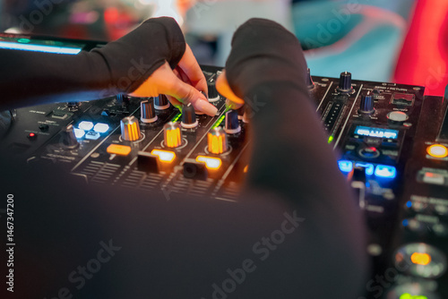 Obraz na płótnie A DJ's hands adjust knobs and sliders on a professional audio mixer, surrounded by illuminated buttons and controls, creating an engaging atmosphere for music mixing. w salonie