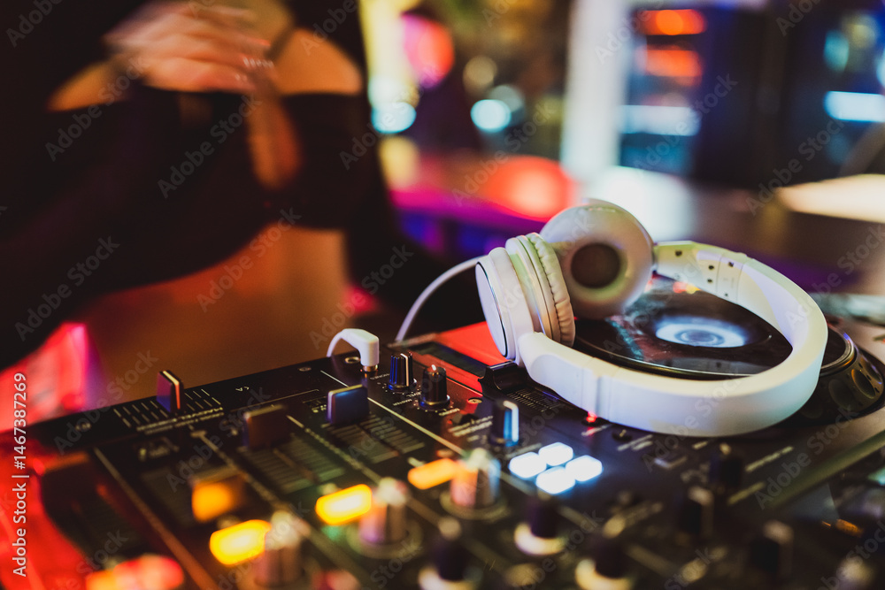Professional DJ mixing console with white headphones resting on it, illuminated by colorful lights. A vibrant club atmosphere, music equipment, and nightlife energy captured in detail.