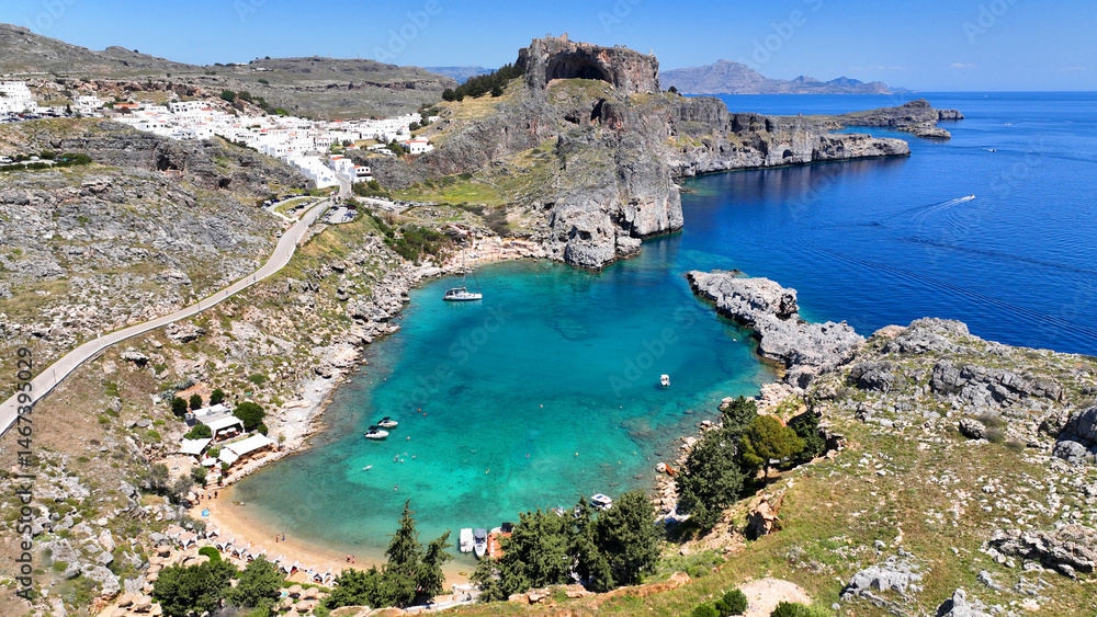 Obraz premium Aerial drone photo of stunning crystal clear sea and small organized beach of Saint Paul's bay overlooked by archaeological site of Acropolis of Lindos, Rhodes island, Dodecanese, Greece