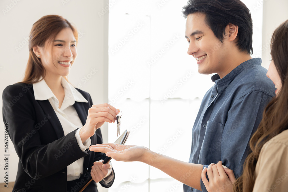 Fototapeta premium Young Asian man receiving house key from female realtor with handshake, showing professional transaction, trust in real estate service, successful deal, and commitment in property ownership