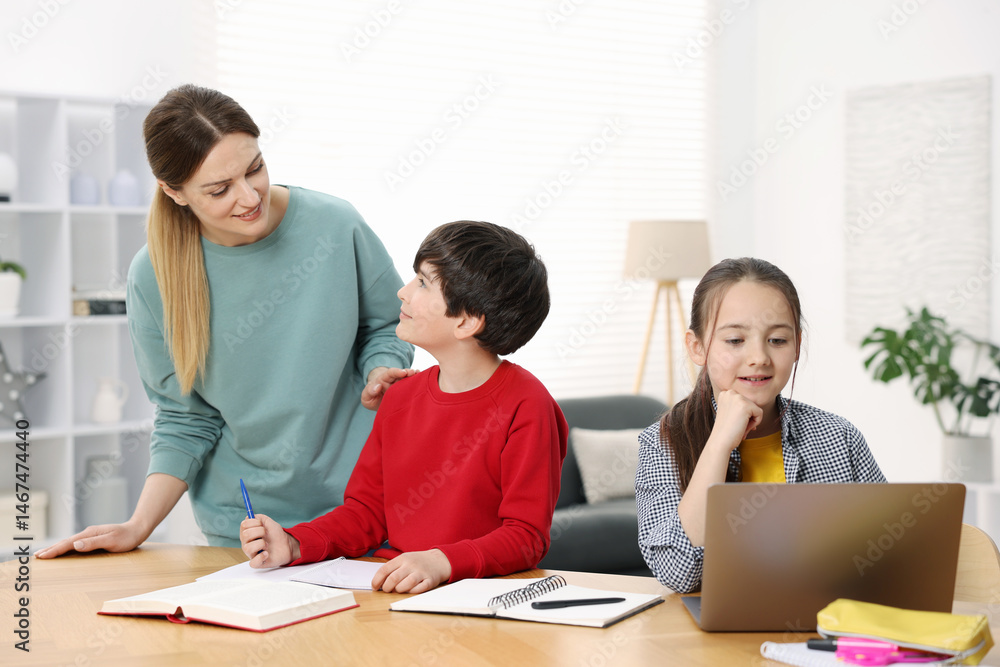 Mother helping her kids with homework at wooden table indoors Mother helping her kids with homework at wooden table indoors