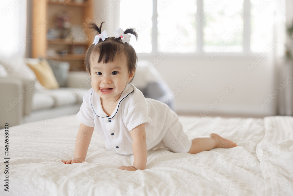 Cheerful baby girl crawling on soft bed in bright living room, wearing cute outfit with bows in her hair and smiling at the camera Cheerful baby girl crawling on soft bed in bright living room, wearing cute outfit with bows in her hair and smiling at the camera