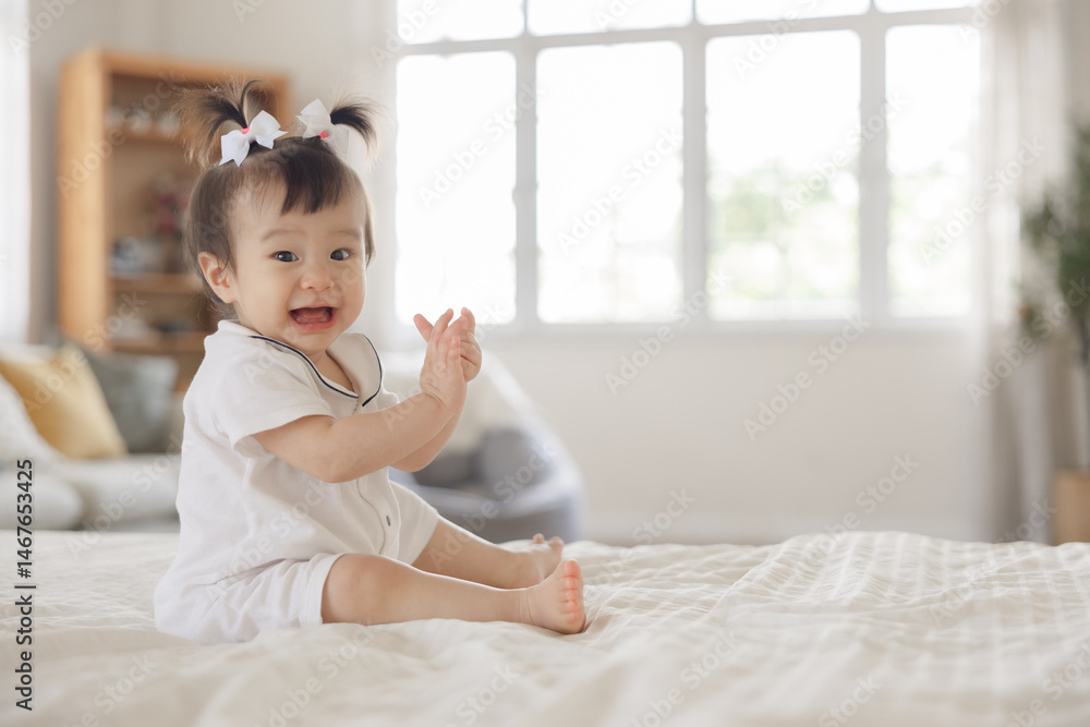 Adorable baby girl with playful expression sitting on cozy bed in well-lit room, enjoying joyful moment and clapping hands with happiness Adorable baby girl with playful expression sitting on cozy bed in well-lit room, enjoying joyful moment and clapping hands with happiness