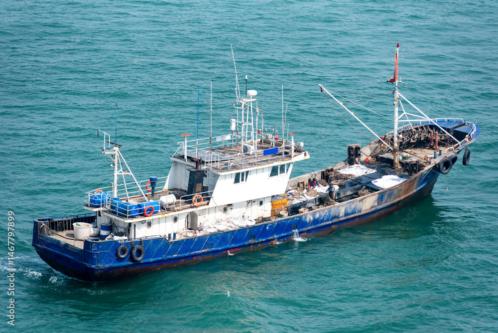 A blue and white fishing boat sails on a calm sea, with gentle waves. The vessel features a deck equipped with fishing gear and a visible wheelhouse. A blue and white fishing boat sails on a calm sea, with gentle waves. The vessel features a deck equipped with fishing gear and a visible wheelhouse.