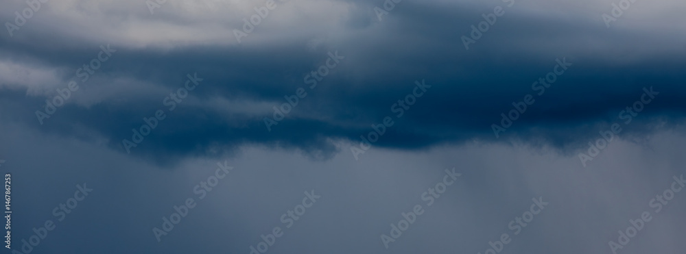 Fototapeta premium Thick storm clouds stretch across the sky with a visible curtain of rain falling below, creating a dramatic and moody atmosphere ample copy space.