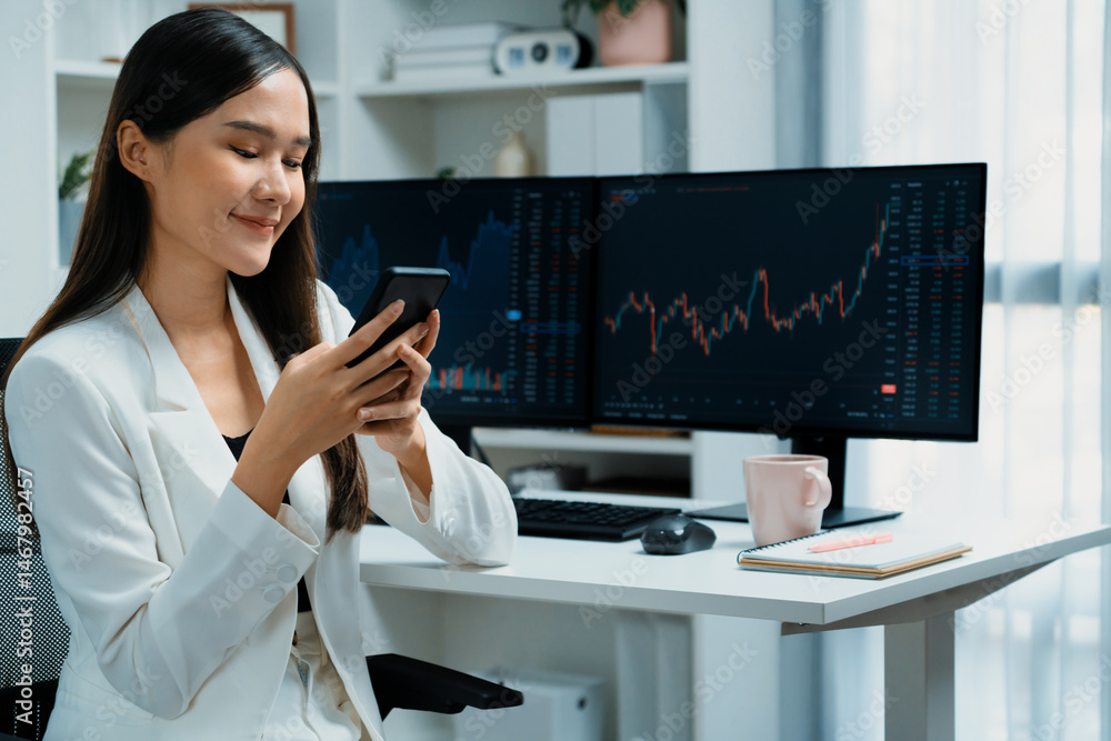 Smiling young Asian businesswoman with happy face looking on smartphone in profitable of exchange stock market graph at modern office. Concept of investing high profit in wealth security. Stratagem. Smiling young Asian businesswoman with happy face looking on smartphone in profitable of exchange stock market graph at modern office. Concept of investing high profit in wealth security. Stratagem.