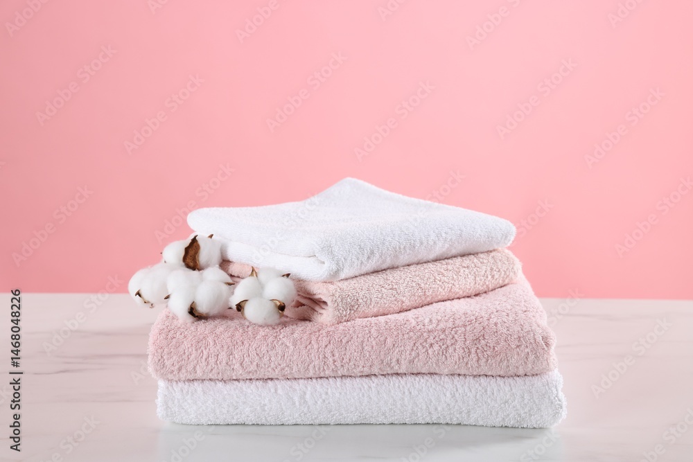 Stack of clean towels and cotton flowers on light marble table against pink background Stack of clean towels and cotton flowers on light marble table against pink background