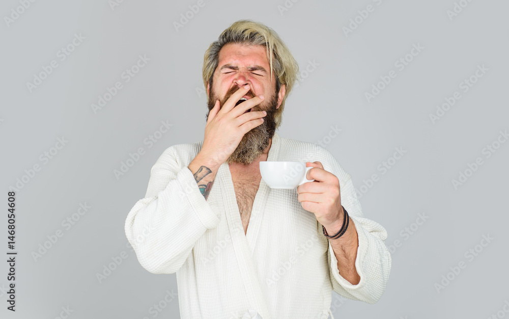 Sleepy yawning man with cup of tea or coffee. Morning refreshment. Sleepy bearded man in bathrobe with cup of hot drink. Tired handsome man with sleepy face trying to wake up with cup of fresh coffee. Sleepy yawning man with cup of tea or coffee. Morning refreshment. Sleepy bearded man in bathrobe with cup of hot drink. Tired handsome man with sleepy face trying to wake up with cup of fresh coffee.