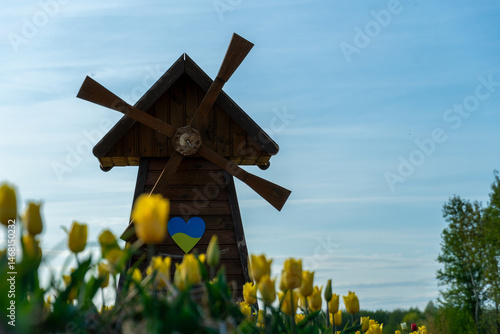 Windmill stands behind yellow tulips with a blue and yellow heart on the side against the sky.