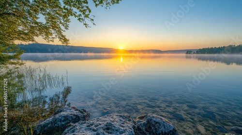 Serene sunrise over a calm lake, with mist rising over the water, and trees on the shore.