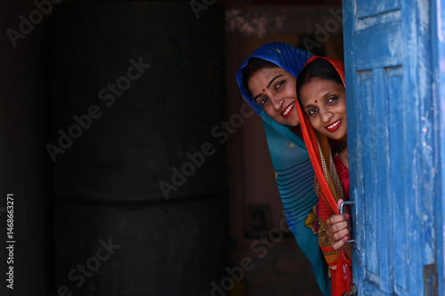Portrait of Indian poor rural women from village in colorful traditional saree standing outside their home.