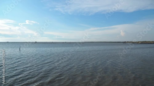 Timelapse of white clouds, blue sky, a quiet seaside or waterfront.