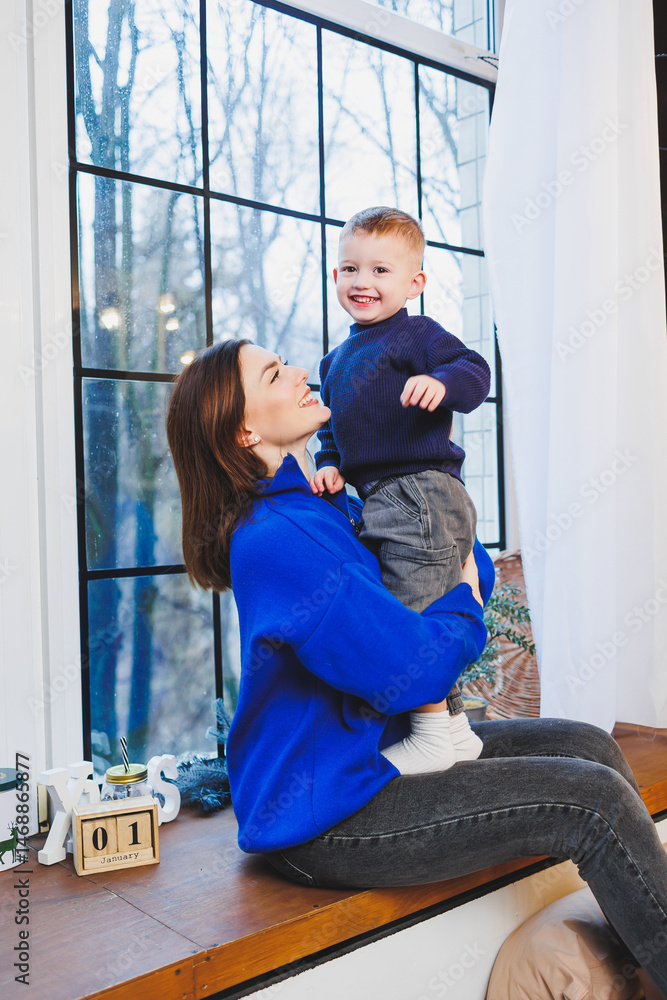 Happy mother and her 4 year old son hugging while sitting on the windowsill at home. Trusting relationship between mother and son. Little boy hugging his mother.