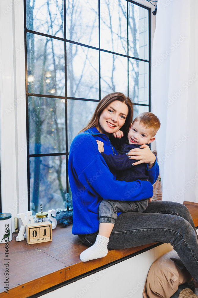 Happy mother and her 4 year old son hugging while sitting on the windowsill at home. Trusting relationship between mother and son. Little boy hugging his mother.
