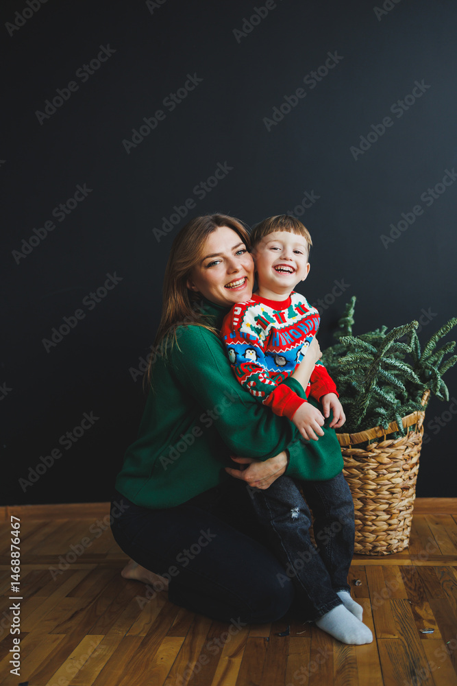 Mother and little son at home on Christmas, child smiles at mother, congratulates and gives unexpected gift. Woman mother receives gift from son on birthday. Family holiday, love concept