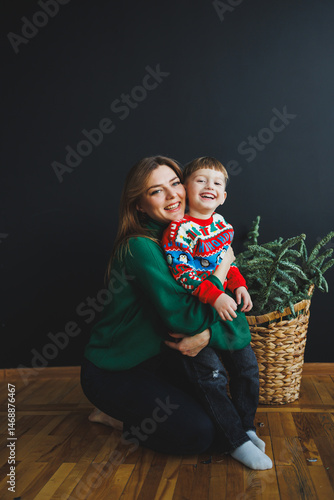 Obraz na płótnie Mother and little son at home on Christmas, child smiles at mother, congratulates and gives unexpected gift. Woman mother receives gift from son on birthday. Family holiday, love concept w salonie