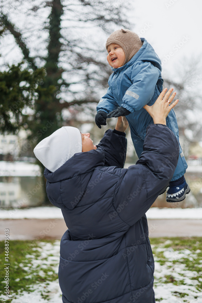 Smiling mother playing with her one-year-old son on the street. Child development and active recreation. Toddler boy playing with his mother on the playground.