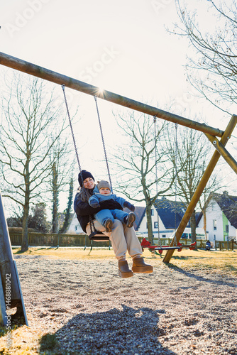 Obraz na płótnie Smiling mother playing with her one-year-old son on the street. Child development and active recreation. Toddler boy playing with his mother on the playground. w salonie