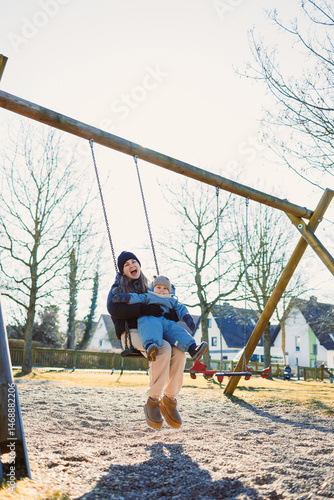 Obraz na płótnie Smiling mother playing with her one-year-old son on the street. Child development and active recreation. Toddler boy playing with his mother on the playground. w salonie