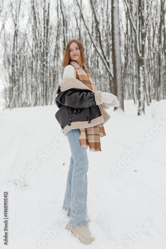Obraz na płótnie Happy smiling young woman wearing coat, scarf, and mittens enjoying winter weather while walking in snowy winter park. Stylish winter women's clothing. w salonie