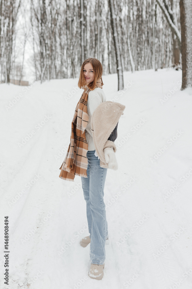 Pretty woman in a fur coat with a big warm scarf around her neck on a winter walk. Woman smiles and rejoices in the snow in winter. Girl walks through a snowy park in winter.