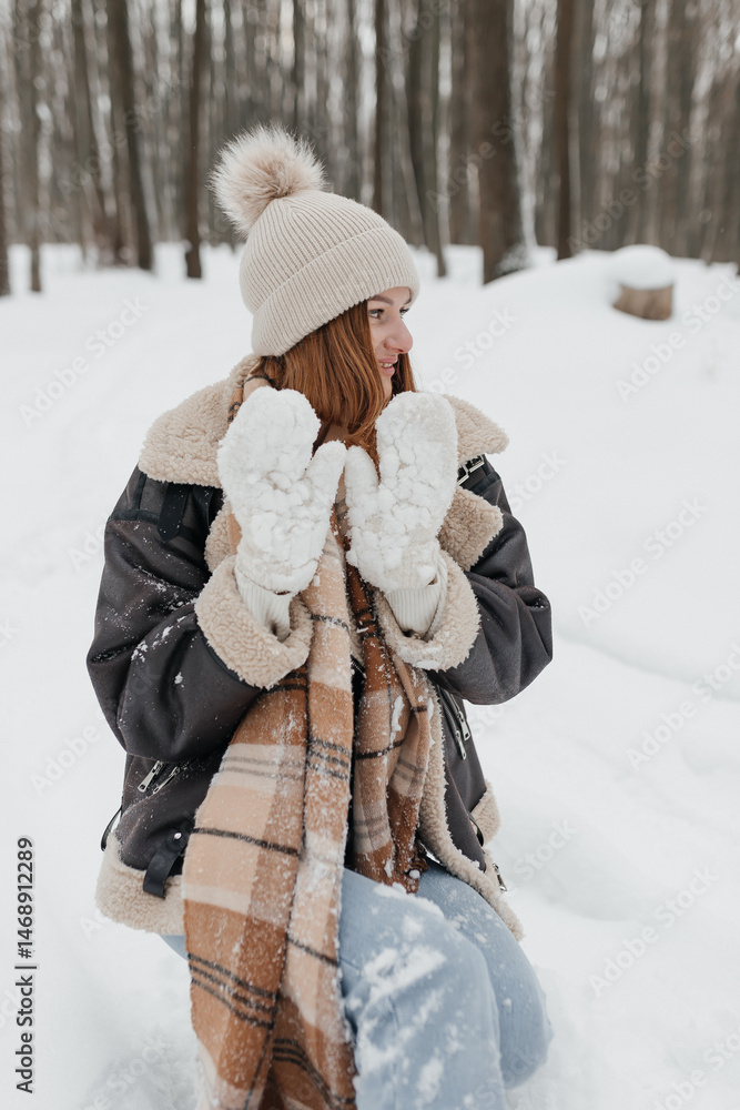 Pretty woman in a fur coat with a big warm scarf around her neck on a winter walk. Woman smiles and rejoices in the snow in winter. Girl walks through a snowy park in winter.