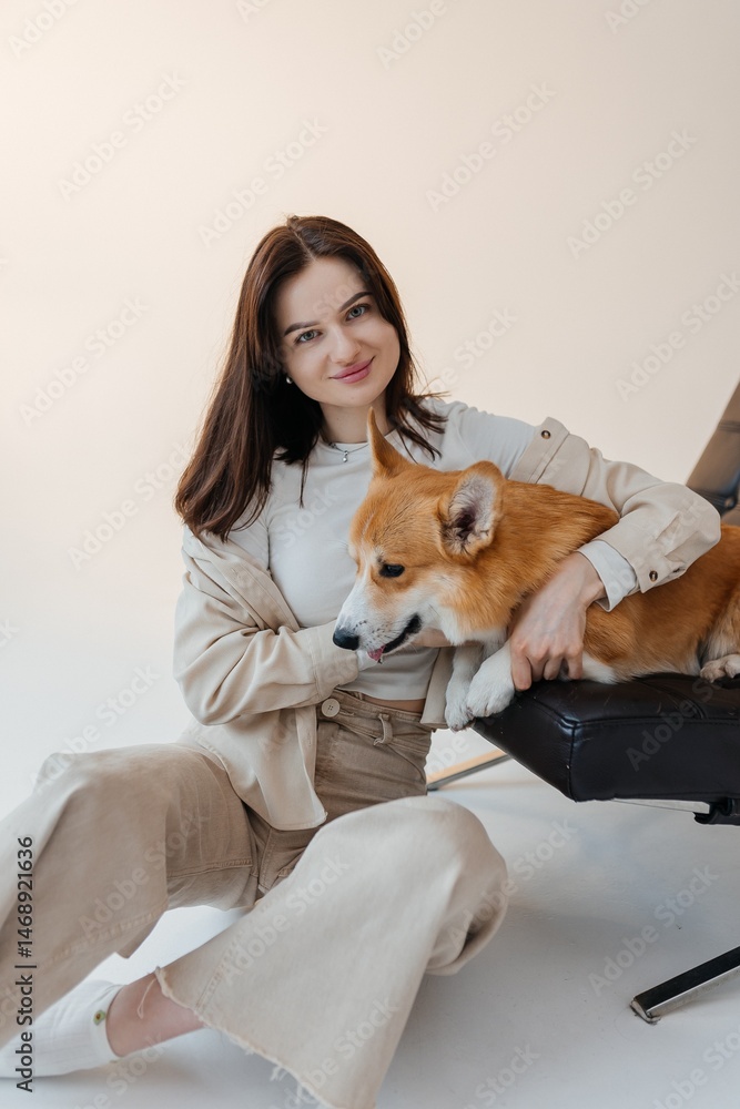 Woman in jeans sitting on the floor and playing with a corgi dog. Cute brunette woman in a white t-shirt and jeans hugging a corgi on a white background. Love for animals. woman holding a corgi dog.