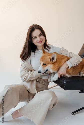 Obraz na płótnie Woman in jeans sitting on the floor and playing with a corgi dog. Cute brunette woman in a white t-shirt and jeans hugging a corgi on a white background. Love for animals. woman holding a corgi dog. w salonie