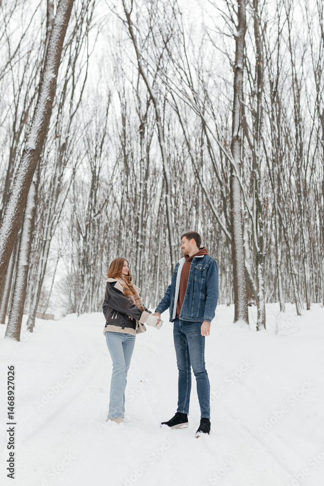 Happy couple in love on a walk in a winter park. Smiling couple holding hands walking through a snowy forest.