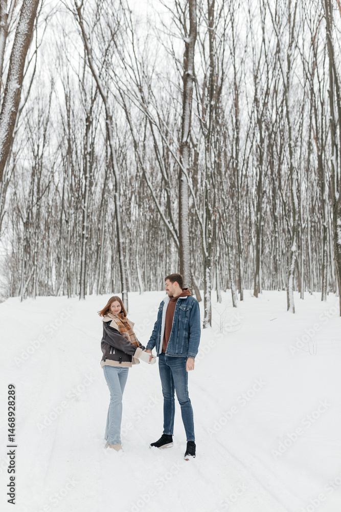A couple in love on a walk in a snowy winter park. A walk in the winter forest of two happy people. A guy and a girl holding hands and hugging.