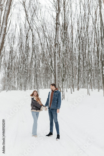Obraz na płótnie A couple in love on a walk in a snowy winter park. A walk in the winter forest of two happy people. A guy and a girl holding hands and hugging. w salonie
