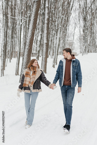 Obraz na płótnie Happy couple in love on a walk in a winter park. Smiling couple holding hands walking through a snowy forest. w salonie
